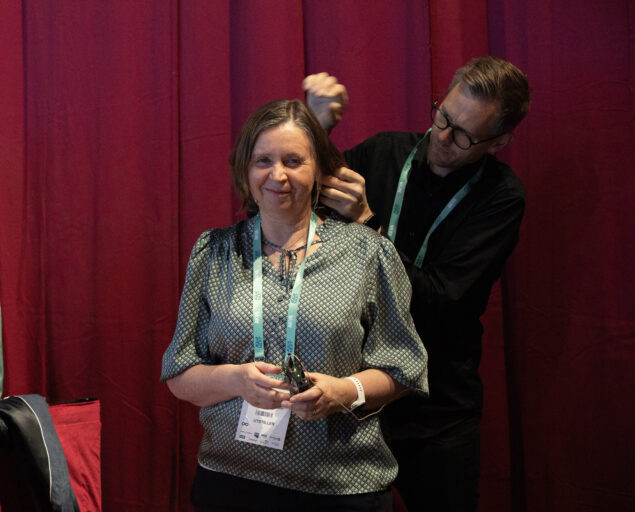 Thomas Hovmøller Ris, Anne Ingeborg Myhr gjør seg klar for å presentere, Anne Myhr gjør seg klar, <p>Thomas Hovmøller Ris, NORCE</p>, En mann setter hodemikron på en kvinne.