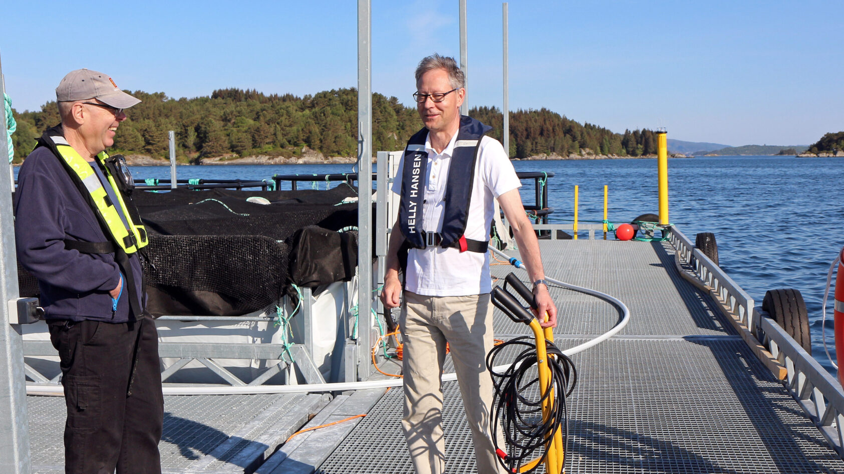 Ingvar Henne, Erik Bjerke fra Kongsberg Discovery og Anders Vahlin, NORCE tester ut smarte sensorer og nettverkskommunikasjon under vann i sanntid, på Havforskningsinstituttet sin forskningsstasjon på Austevoll., Jakter gåten på havets tilstand med ny teknologi, <p>Ingvar Henne, leder SFI Smart Ocean</p>, To smilende karer på en brygge i solskinn.