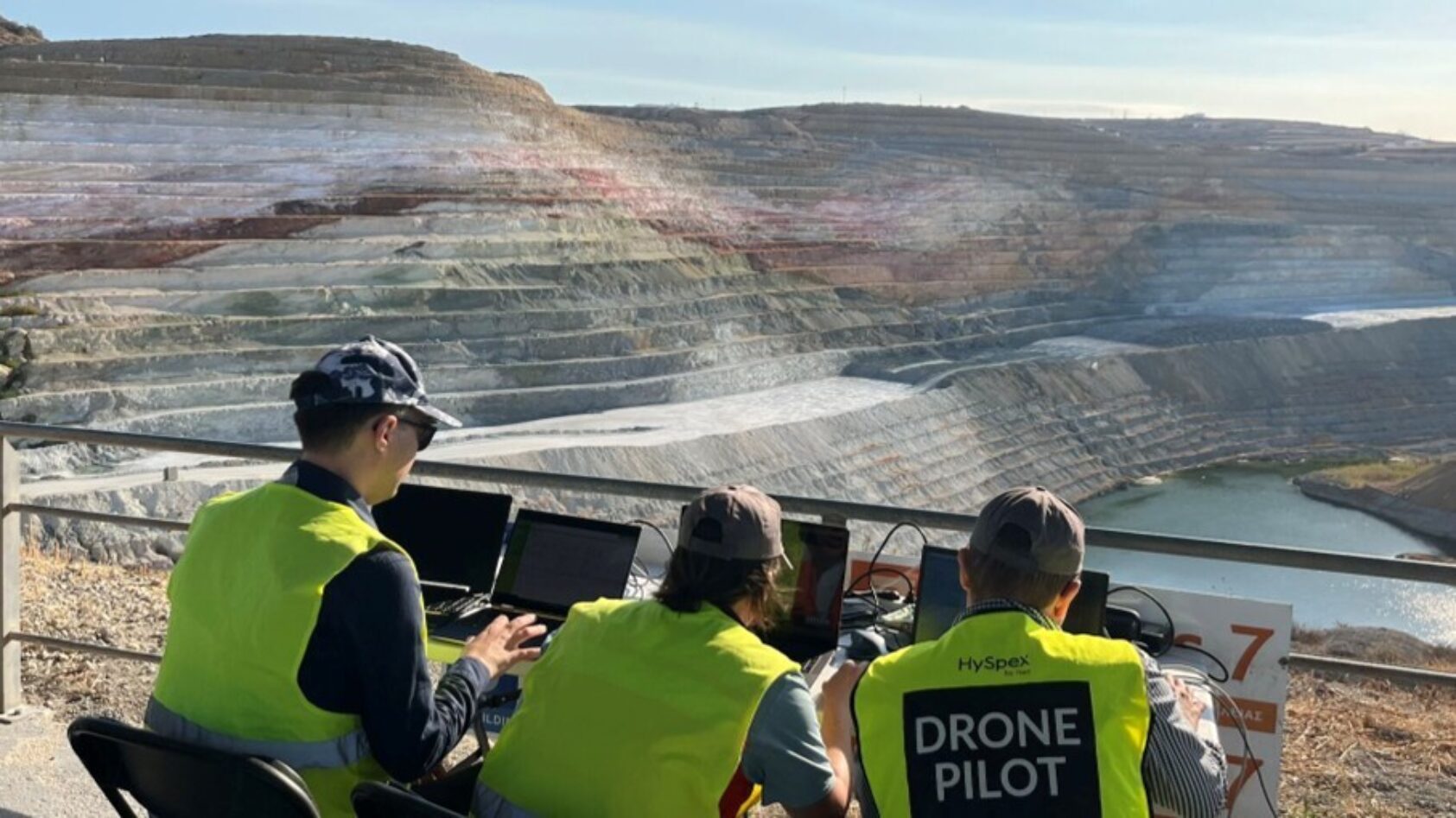 NEO, Drone pilots flying a drone equipped with a hyperspectral camera from Norsk Elektro Optikk AS. Data was collected data from a bentonite mine in Greece for the EU project M4Mining. In the picture, you see (from left) Axel Fredrik Bohman, Friederike Körting, and Justus Constantin Hildebrand, all from NEO., M4minig NEO, , Three persons outdoor by a table with computers, an open mine in the background