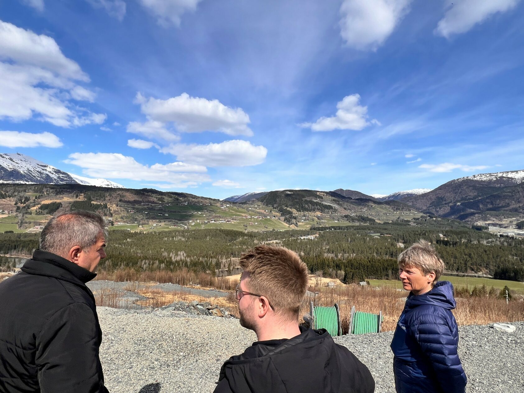 Gunn Janne Myrseth, NORCE, Bømoen sett fra Skutleåsen med COWI-guide Christian Rekve Bryn i midten og omkranset av forskerne Todoz Belezhkov fra Energy Agency of Plovdiv i Bulgaria og NORCE-forsker Kirsti Midttømme.både, Utsikt, <p>Gunne Janne Myrseth, NORCE.</p>, Tre mennseker beundrer utsikten mot fjellene, sol og lettskyet himmel over fjellene.