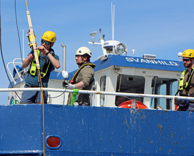 Ingvar Henne, Ulike sensorer synkes ned av Jean-Baptiste Danre, Havforskningsinstituttet, Rune Øyerhamn, NORCE sammen med Erik Bjerke, Kongsberg Discovery og Roald Otnes, FFI, 2, <p>Ingvar Henne</p>, Tre karer ved båtripa, den ene håndterer en wire med utstyr.