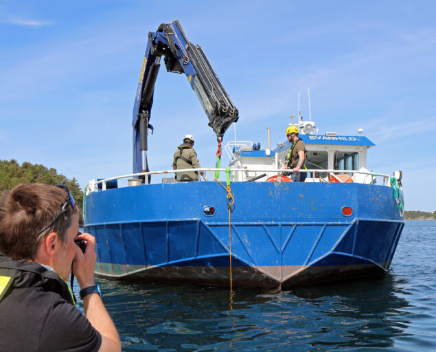 Ingvar Henne, Fotograf Frode Ims med fokus fra kaia., 4, <p>Ingvar Henne</p>, Fotograf tar bilde av en liten kranbåt på sjøen.